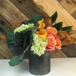 Arrangement of orange roses, yellow calla lilies, and green hydrangeas in a dark vase