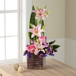 Pink lilies and mixed purple flowers in a wooden cube vase