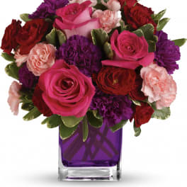 Compact mix of pink roses and red and purple carnations in a square purple glass vase