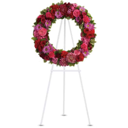 Standing circular wreath of red and pink flowers displayed on a white metal easel