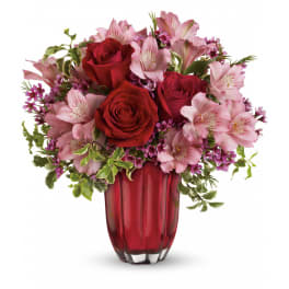 Arrangement of red roses and pink alstroemeria in a red glass vase with small purple blooms