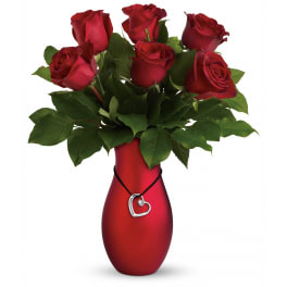 Red roses arranged in a red vase with a heart pendant accent.