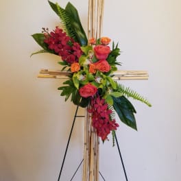 Floral cross arrangement with pink roses and red orchids on a bamboo stand