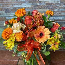 Orange and yellow mixed bouquet in a glass vase with a ribbon