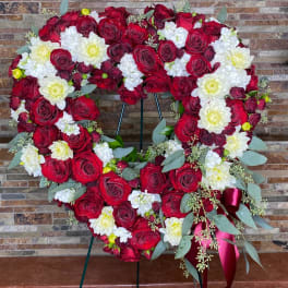 Heart-shaped floral wreath of red roses and white flowers on a stand