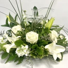 White roses and lilies arranged around a clear glass cross