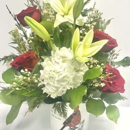 Red roses and white lilies in a white vase with a hydrangea bloom