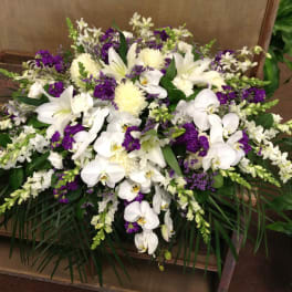 White orchids and lilies arranged with purple flowers in a low spray.
