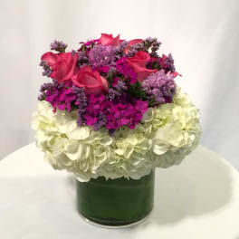 Pink roses and purple flowers in a green glass vase with white hydrangeas