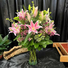 Pink lilies and small purple flowers arranged in a glass vase
