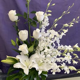 White roses, lilies, and orchids arranged in a tall vase