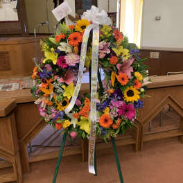 Large colorful funeral wreath on an easel with white ribbons