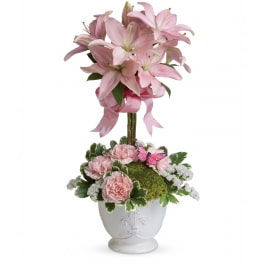 Topiary-style arrangement of pink lilies and carnations in a white ceramic pot with moss and a pink butterfly.