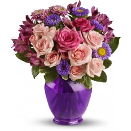 Pink roses with purple accent flowers arranged in a glossy purple vase