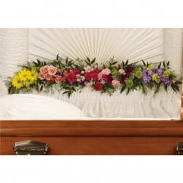 Mixed casket floral spray of bright roses and other blooms against white fabric lining