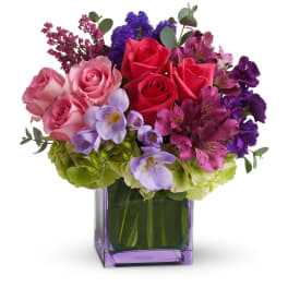 Colorful arrangement of pink roses and purple flowers in a square lavender glass vase