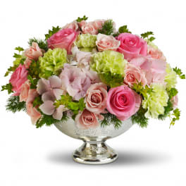 Low arrangement of pink roses, green carnations, and pale hydrangeas in a silver pedestal bowl