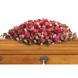Pink and red casket spray of mixed flowers on a light wood casket