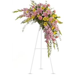 Standing spray of pink lilies, carnations, and yellow daisies on a white easel.