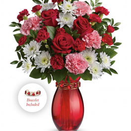 Red, pink, and white bouquet with roses, carnations, and mums in a red vase with a decorative bracelet