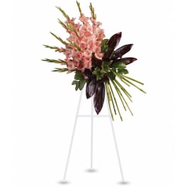 Standing spray of pink gladiolus-style flowers with dark foliage on a white easel