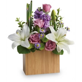 Modern arrangement of white lilies, pink roses, and purple flowers in a rectangular bamboo box