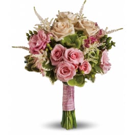 Hand-tied bouquet of blush pink and cream roses with accent blooms, wrapped in pink ribbon.