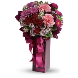 Tall pink vase arrangement with red roses, pink carnations, and purple mums tied with a satin bow