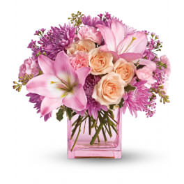 Pink lilies, peach roses, and purple mums arranged in a pink glass cube vase