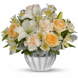 Low arrangement of white lilies, peach roses, and cream carnations in a silver bowl vase
