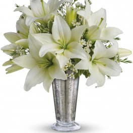 Tall silver vase filled with white lilies and small white filler flowers in a compact arrangement
