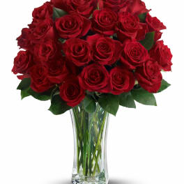 Tall clear vase filled with a large bouquet of long-stemmed red roses