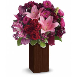 Tall arrangement of pink lilies, red roses, and purple blooms in a dark rectangular vase