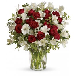 Arrangement of red roses and white alstroemeria in a clear glass vase with variegated foliage.