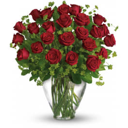 Arrangement of long-stemmed red roses in a clear glass vase with accent filler.