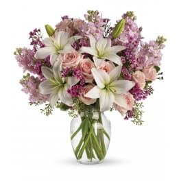 White lilies, pink roses, and purple flowers arranged in a clear glass vase