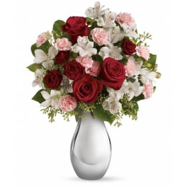 Red roses, pink carnations, and white alstroemeria in a shiny silver vase