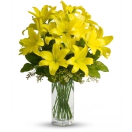 Tall bouquet of bright yellow lilies in a clear rectangular glass vase