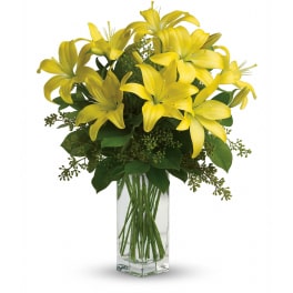 Tall arrangement of yellow lilies in a clear rectangular glass vase
