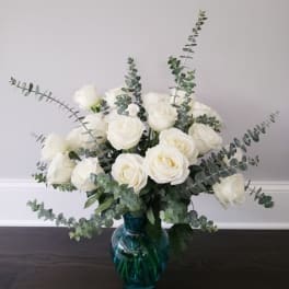 White roses in a blue glass vase with airy eucalyptus stems