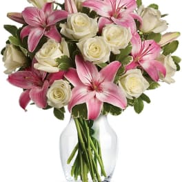 Pink lilies and white roses arranged in a clear glass vase