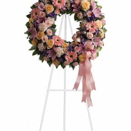 Pastel floral wreath on a white stand with a pink ribbon
