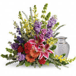 Colorful floral arrangement with lilies, roses, and gerbera daisies beside a decorative urn