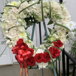 Large floral wreath of white and red roses on an easel with a red bow