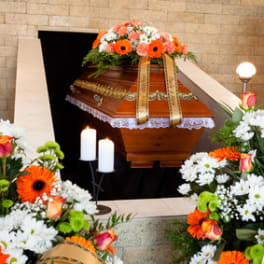 Funeral casket with orange and white floral sprays and candles
