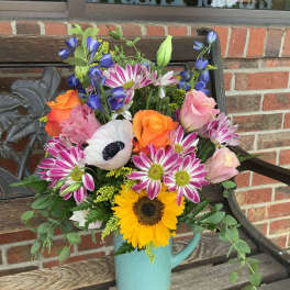 Mixed bouquet in a blue pitcher with sunflowers, roses, and daisies