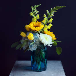Yellow sunflowers and white blooms in a blue glass vase