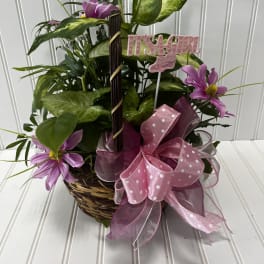 Basket arrangement with purple flowers, pink ribbon, and a "It's a Girl" pick