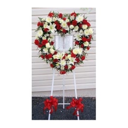 Heart-shaped red and white floral wreath on a stand with red bows