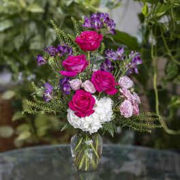 Pink roses and purple flowers arranged in a glass vase